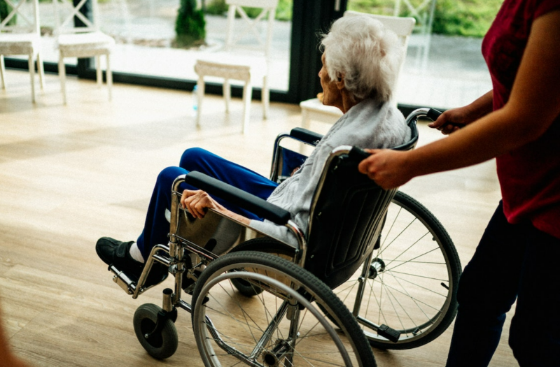 An elderly person seated in a wheel chair, in a nursing home.