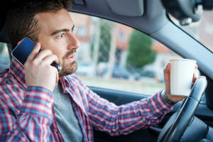 man holding phone and coffee while driving 