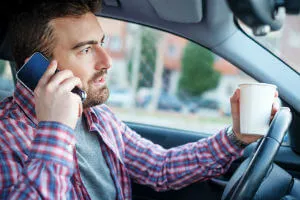 man holding phone and coffee while driving